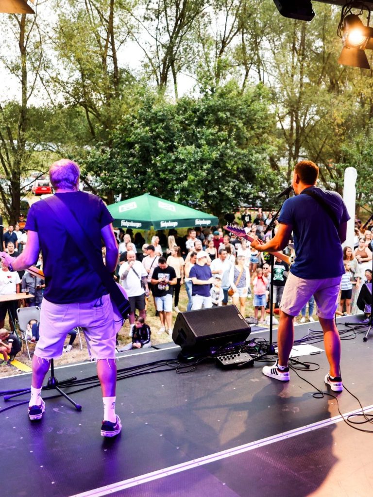 Zwei Musiker spielen live auf einer Bühne vor einem Publikum im Freien.